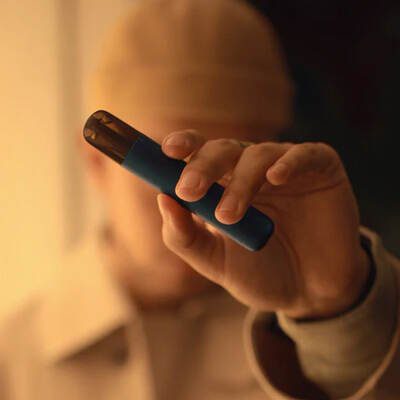 Close-up of a hand holding a blue vape device with a blurred warm-toned background.